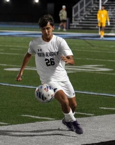 Soccer player in white uniform focused on controlling the ball during a game on a field at night.
