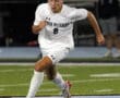 Soccer player in white uniform sprints toward ball on field at night game.
