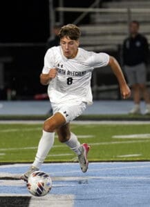 Soccer player in white uniform sprints toward ball on field at night game.