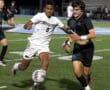 Two soccer players compete for the ball during a night match on a green field.