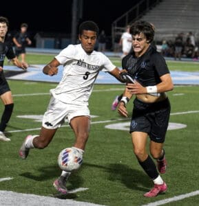 Two soccer players compete for the ball during a night match on a green field.