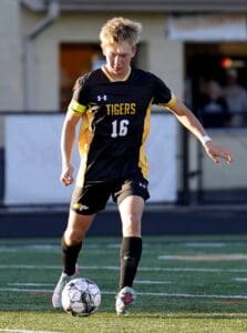 Soccer player in black and yellow jersey dribbling ball on field during a game.