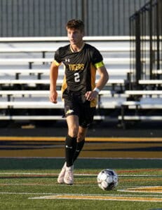 Soccer player in black uniform dribbles ball on field during a sunny day match.