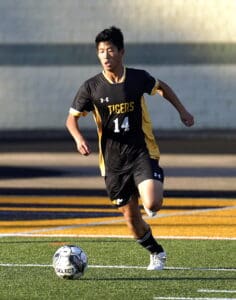 Soccer player in black and yellow kit dribbling ball on field during match.