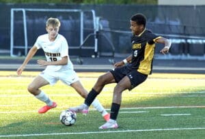 Two soccer players from opposing teams compete for ball control on a grass field during a match.