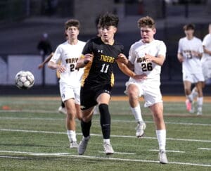 High school soccer match with players from Tigers and Norse teams competing for the ball on the field.