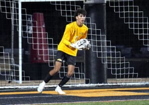 Goalkeeper in yellow jersey holds soccer ball in front of net during night game.