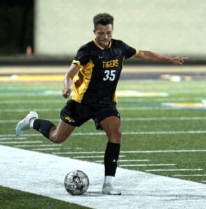 Soccer player in black and yellow jersey kicks ball on green field, wearing number 35.