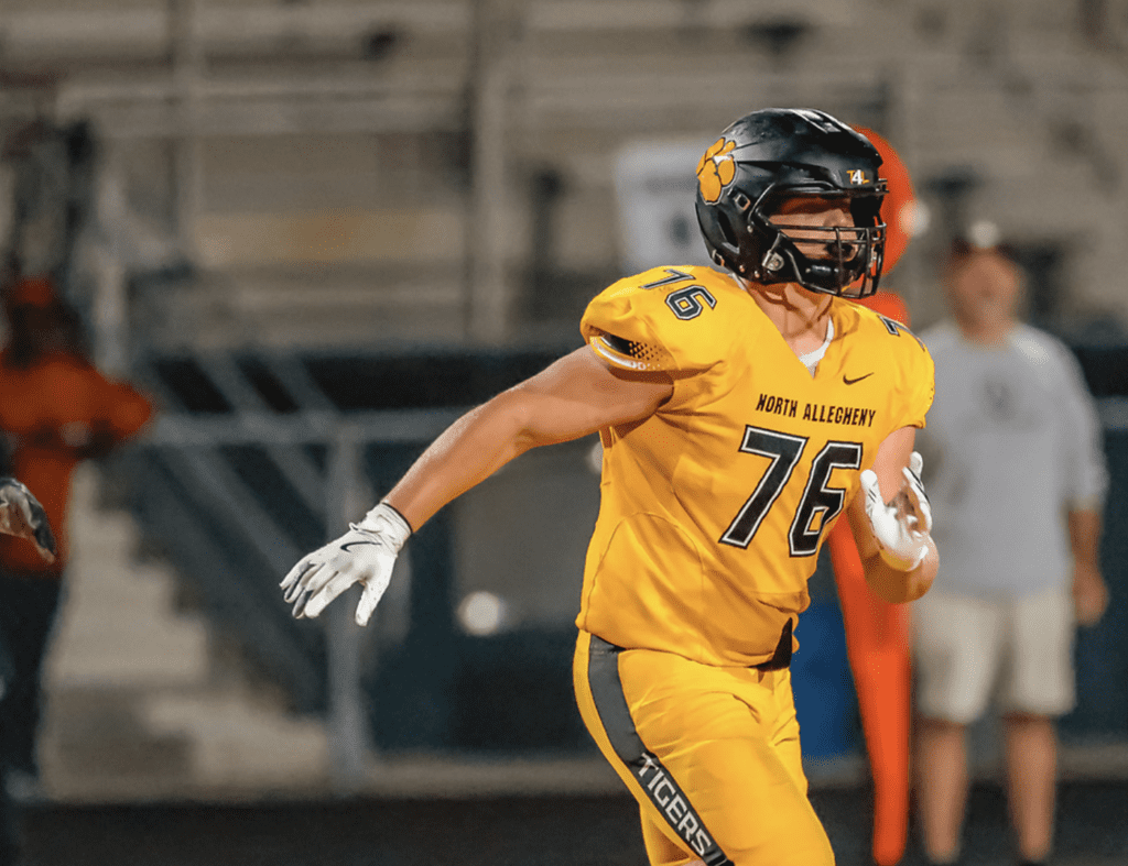 Football player in yellow uniform during a game, wearing a helmet marked with number 76, on the field.