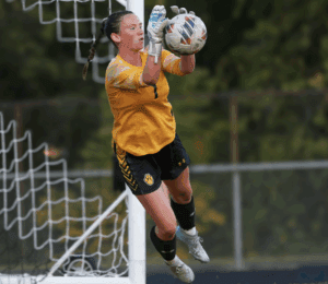 Soccer goalkeeper in action, making a save near the goalpost during a match.