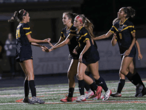 Soccer players in black jerseys celebrate a goal on the field, displaying teamwork and sportsmanship.