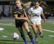 Two female soccer players competing for the ball on a field during a night game.
