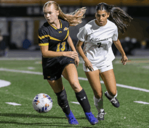 Two female soccer players competing for the ball on a field during a night game.