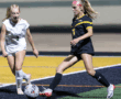 Two female soccer players compete for the ball during a night match on a field with bright yellow lines.