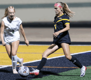 Two female soccer players compete for the ball during a night match on a field with bright yellow lines.