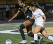 Two female soccer players competing for the ball on a field during a night match.