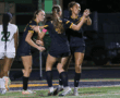 Soccer players in black uniforms celebrate after a goal during a night match on the field.