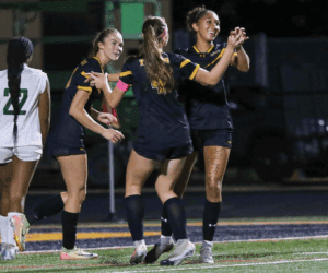 Soccer players in black uniforms celebrate after a goal during a night match on the field.