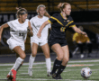 Girls' soccer match action, players in white and black jerseys compete for the ball on the field.