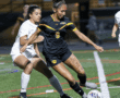 Two female soccer players competing for the ball during a night match, with focus on athletic action and determination.