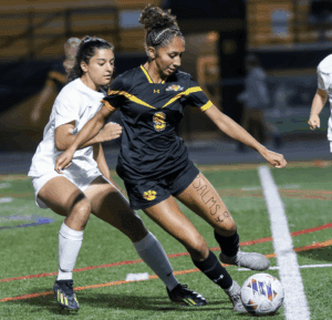 Two female soccer players competing for the ball during a night match, with focus on athletic action and determination.
