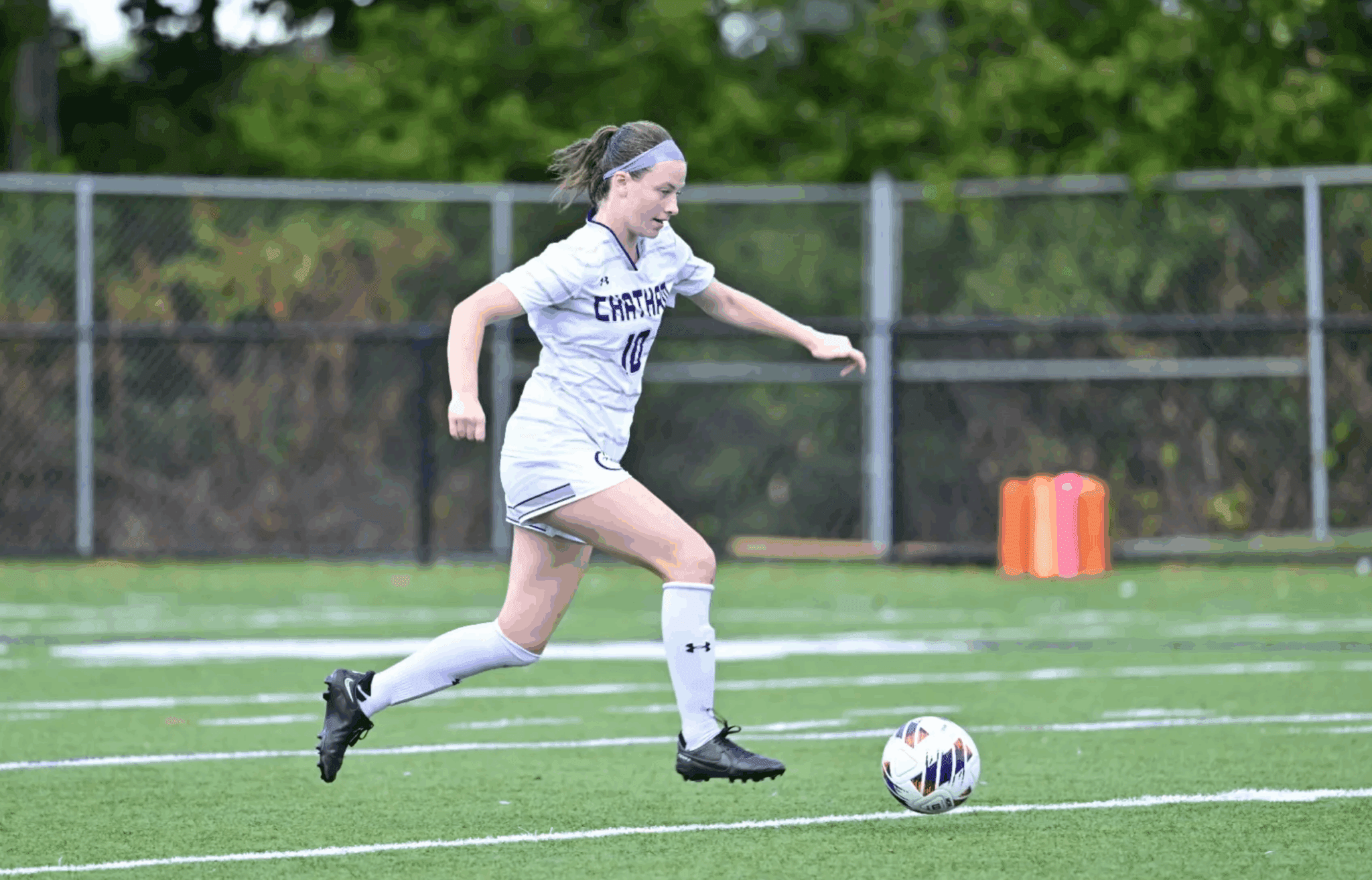 Soccer player in white uniform running towards a soccer ball on a field during a match.