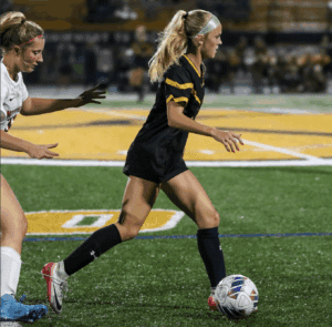 Soccer player in black jersey dribbling the ball on a field during a match.