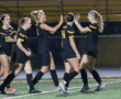 Girls high school soccer team players celebrating on field with high-fives and smiles in black uniforms.