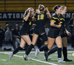 Soccer team celebrates after scoring a goal under stadium lights.