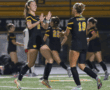 Soccer players in black uniforms celebrating on the field with high-fives during a night game.