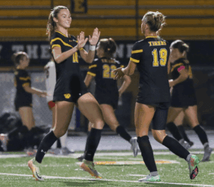 Soccer players in black uniforms celebrating on the field with high-fives during a night game.