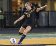 Soccer player in black uniform kicking ball during night game on field.