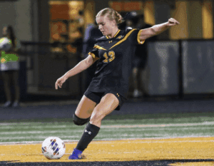 Soccer player in black uniform kicking ball during night game on field.