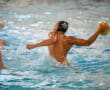 Water polo player in black cap prepares to throw ball in mid-action pool scene, splashing water everywhere.