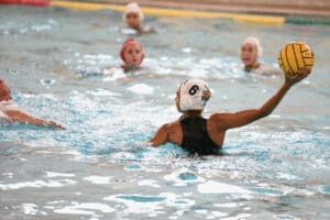 Water polo player preparing to pass the ball during a competitive match in a pool.