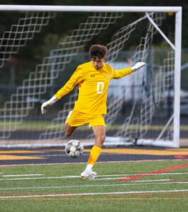 Soccer player in yellow uniform kicks ball on field, focusing on goal post and net in the background.