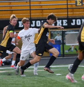 Boys high school soccer match in action, players in black and gold kits challenging for the ball.