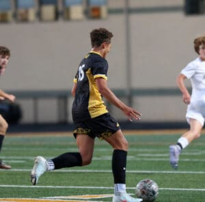 Soccer player in yellow and black uniform dribbling ball during a match, action-packed sports scene on field.