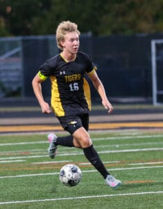 Soccer player in black and yellow uniform dribbling during a match on a field.