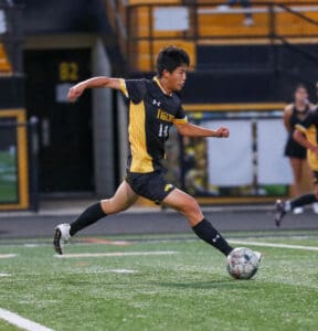 Soccer player in yellow and black jersey running with ball on field during match.