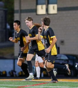 Soccer players in black and yellow uniforms running on the field during a game at dusk.