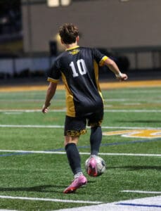 Soccer player in black jersey number 10 dribbling ball on a green field during a nighttime match.