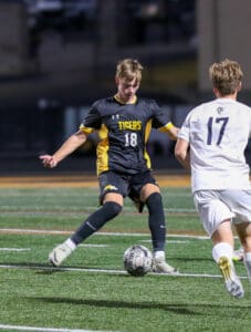 Two soccer players in action during a night game, dribbling on the field, wearing black and white uniforms.