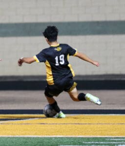 Soccer player in black and yellow jersey kicking ball on field during a game.