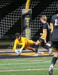 Soccer goalkeeper in yellow diving to save a ball during a night match on a turf field.