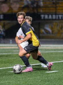 Soccer player in black and yellow kit dribbling during a night match.