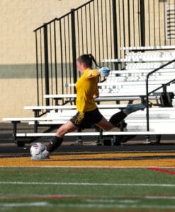 Soccer goalie in yellow jersey kicks ball on field in action shot.