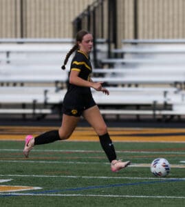 Soccer player dribbling a ball on the field in a black and yellow uniform during a match.