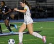 Soccer player in white uniform dribbling the ball during a night game on the field.