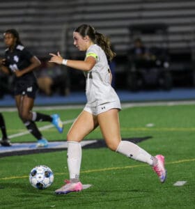Soccer player in white uniform dribbling the ball during a night game on the field.
